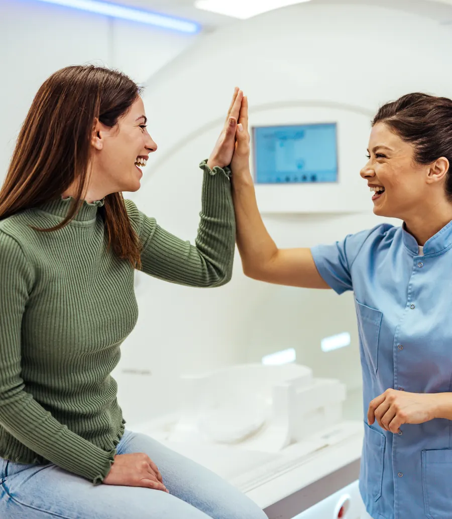 A smiling patient high-fiving her MRI technologist beside the MRI scanner